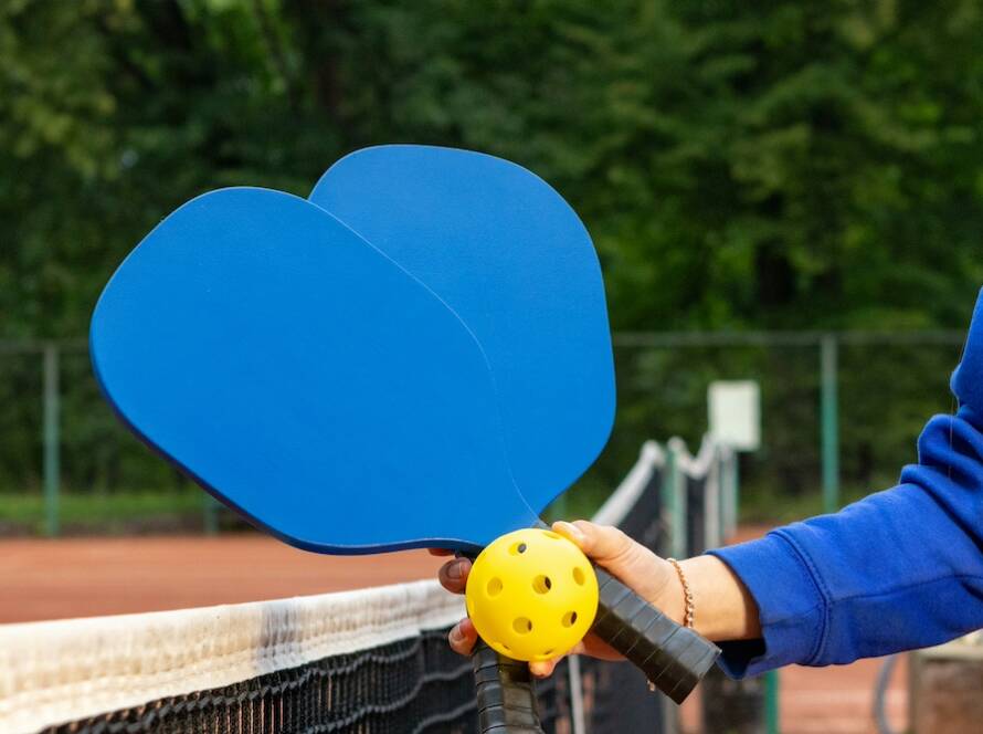 player holding 2 pickleball paddles and balls